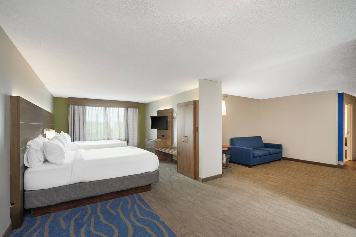 A hotel room with a large bed, a desk, a TV, and a blue sofa.