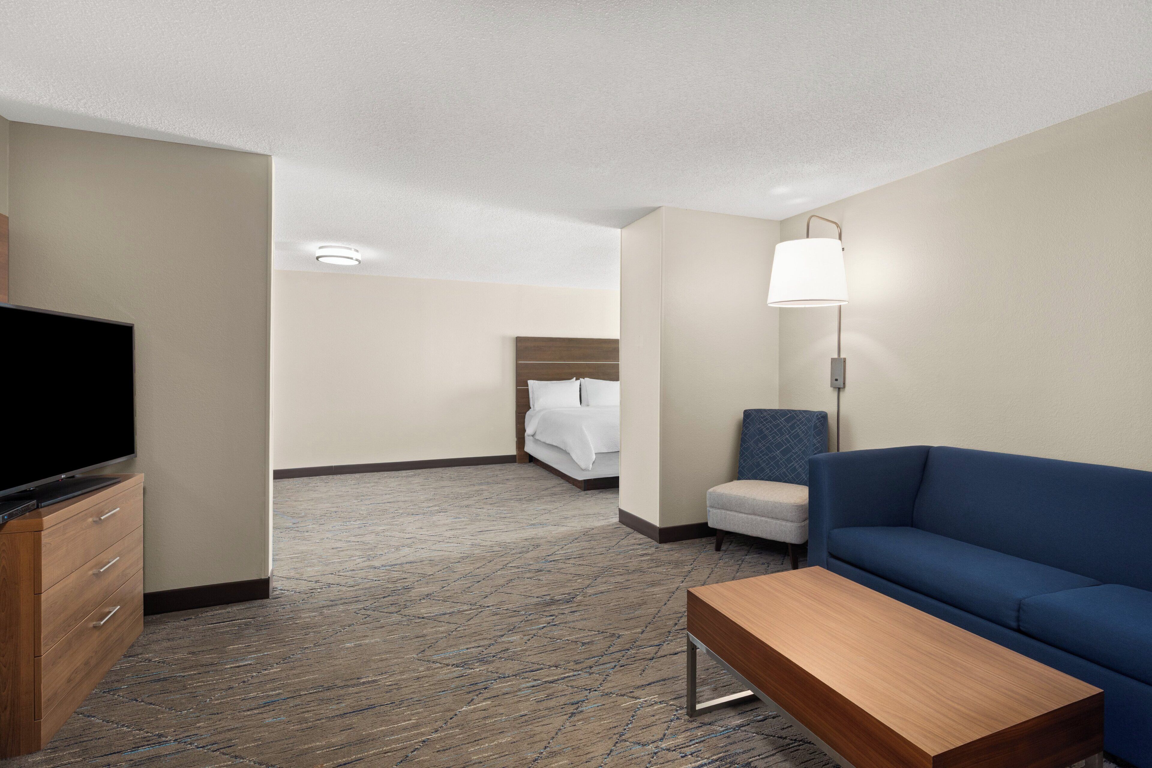 A hotel room with a television, a sofa, a desk, a lamp, and a bed.