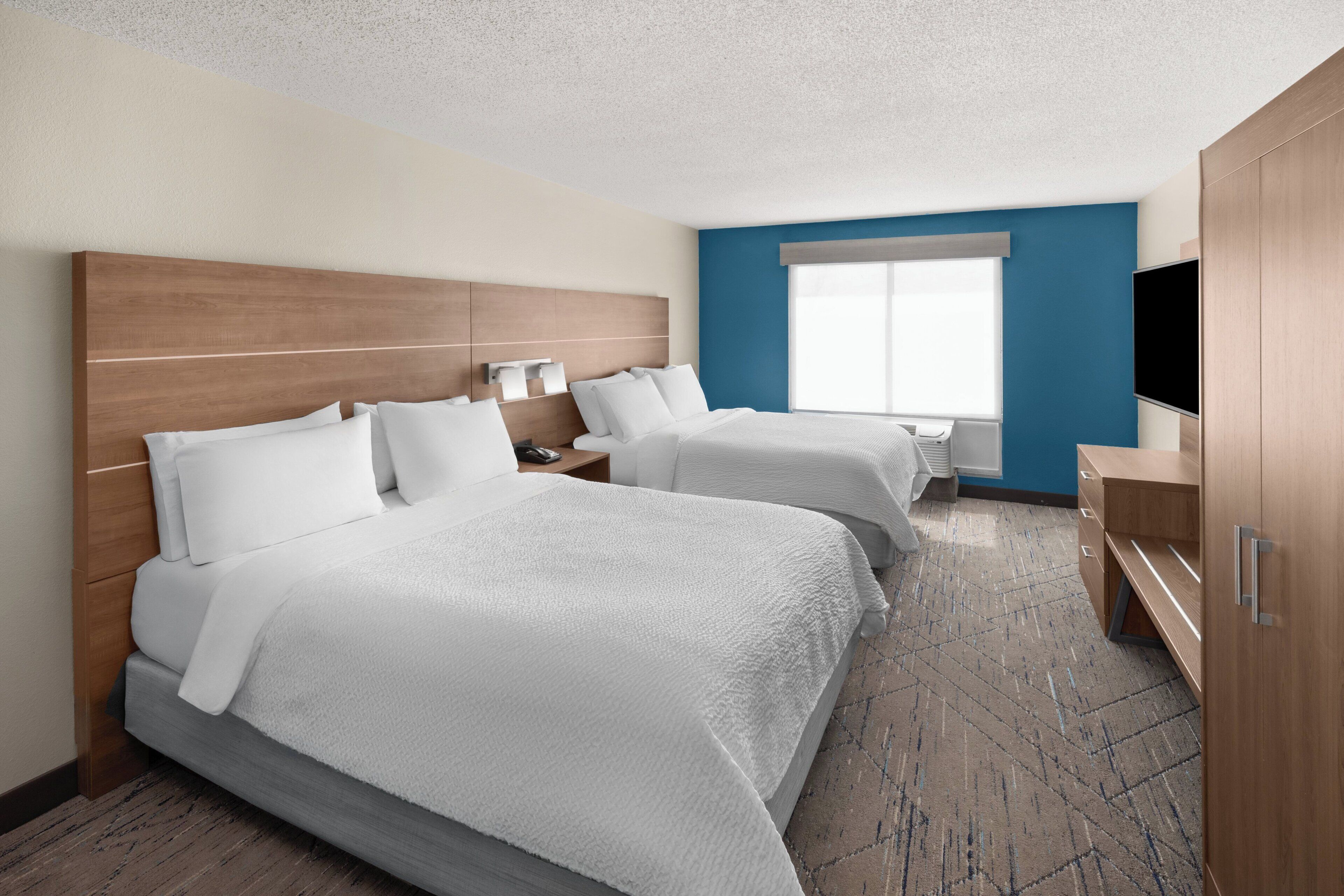 Habitación de hotel con dos camas, un televisor y un ventanal grande.