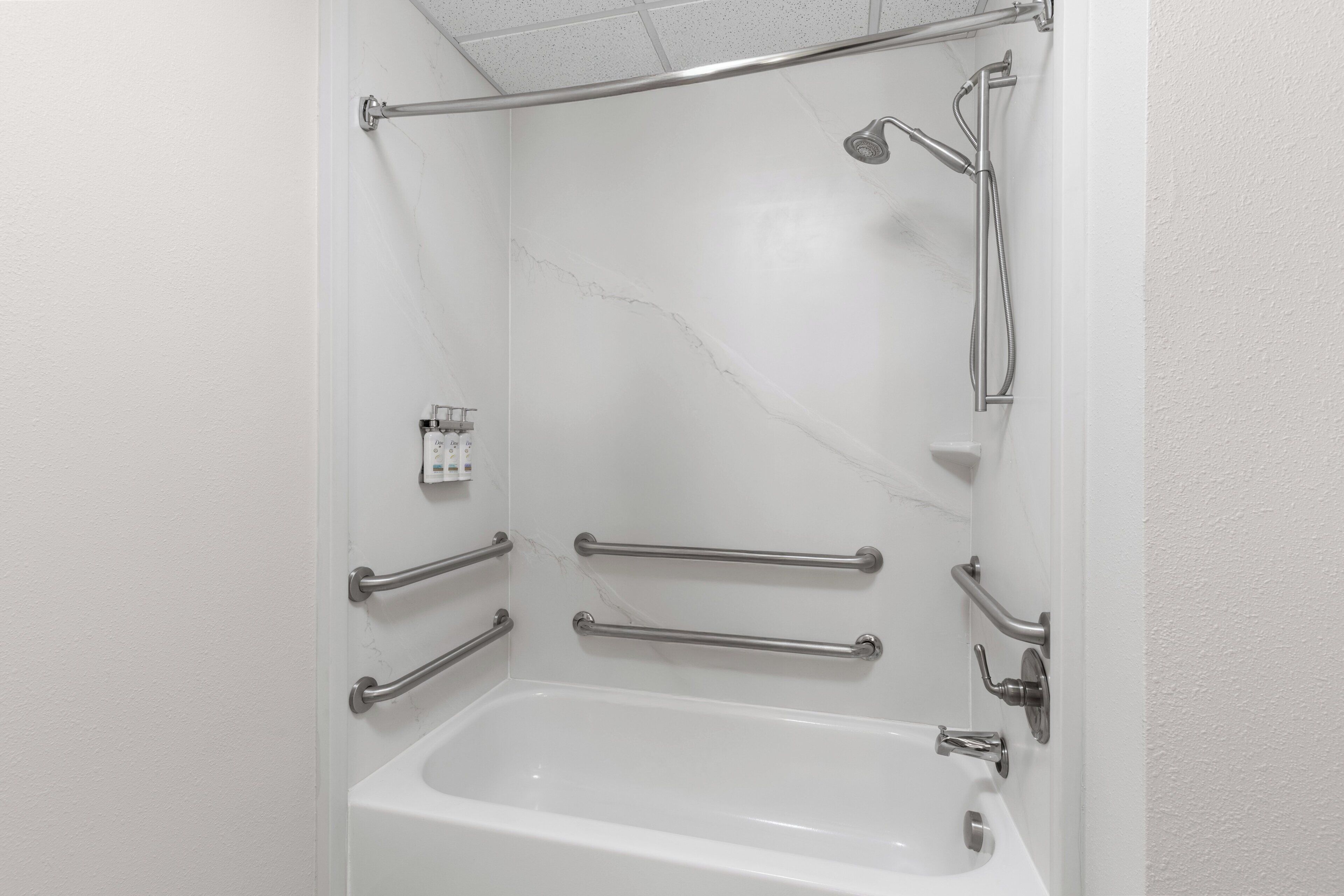 A bathroom with a white bathtub, grab bars, a handheld showerhead, and a handheld shower hose.