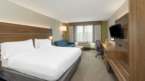 Ein Hotelzimmer mit einem großen Bett, einem Schreibtisch mit Computer, einem Fernseher und einem Fenster mit Vorhängen.