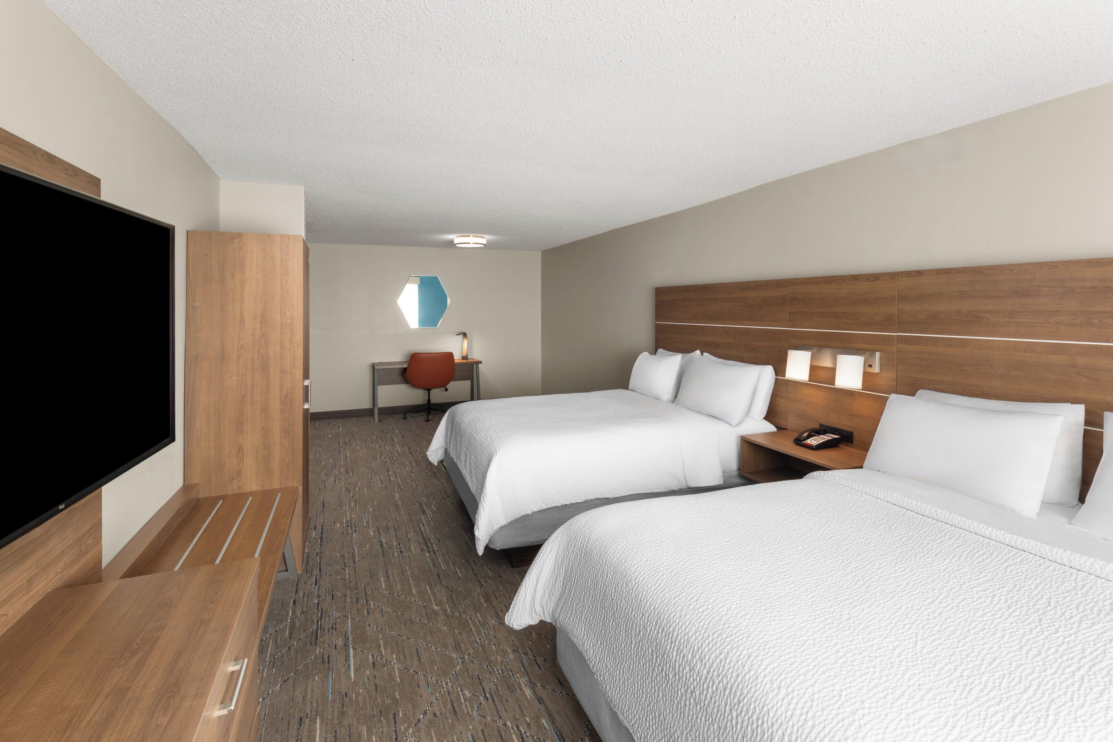 Une chambre d’hôtel avec deux lits, un bureau, une chaise, une télévision et une salle de bain.