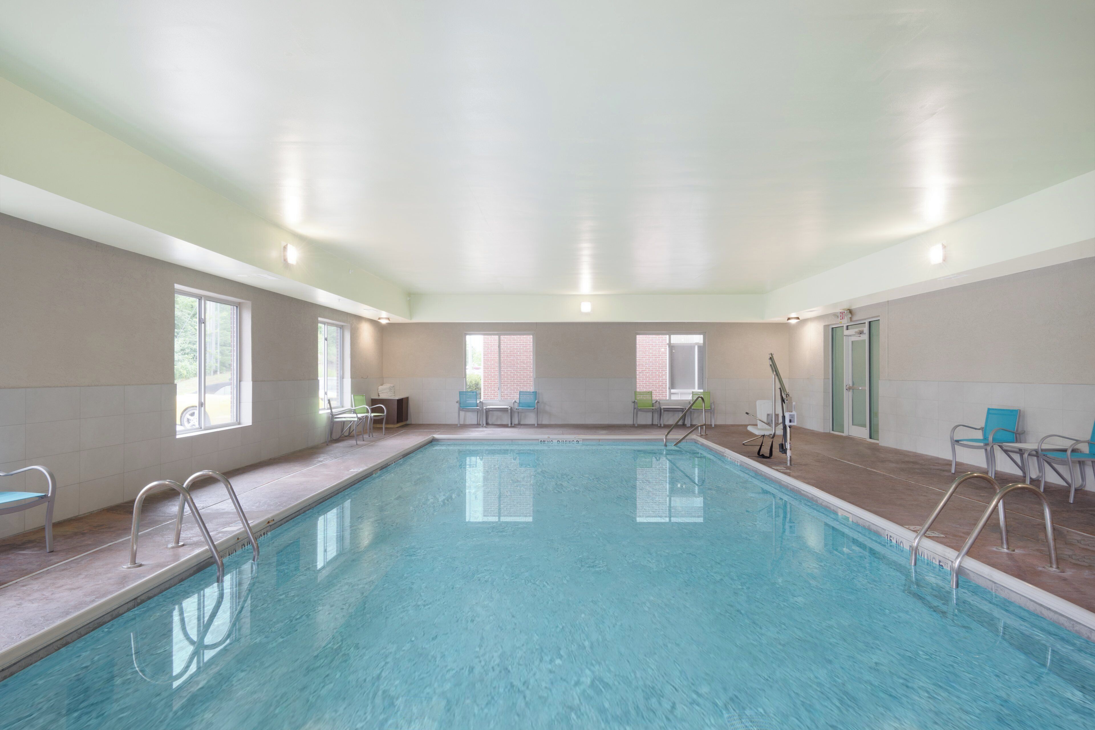 Una amplia piscina interior con agua cristalina, rodeada de paredes de azulejos y ventanas.