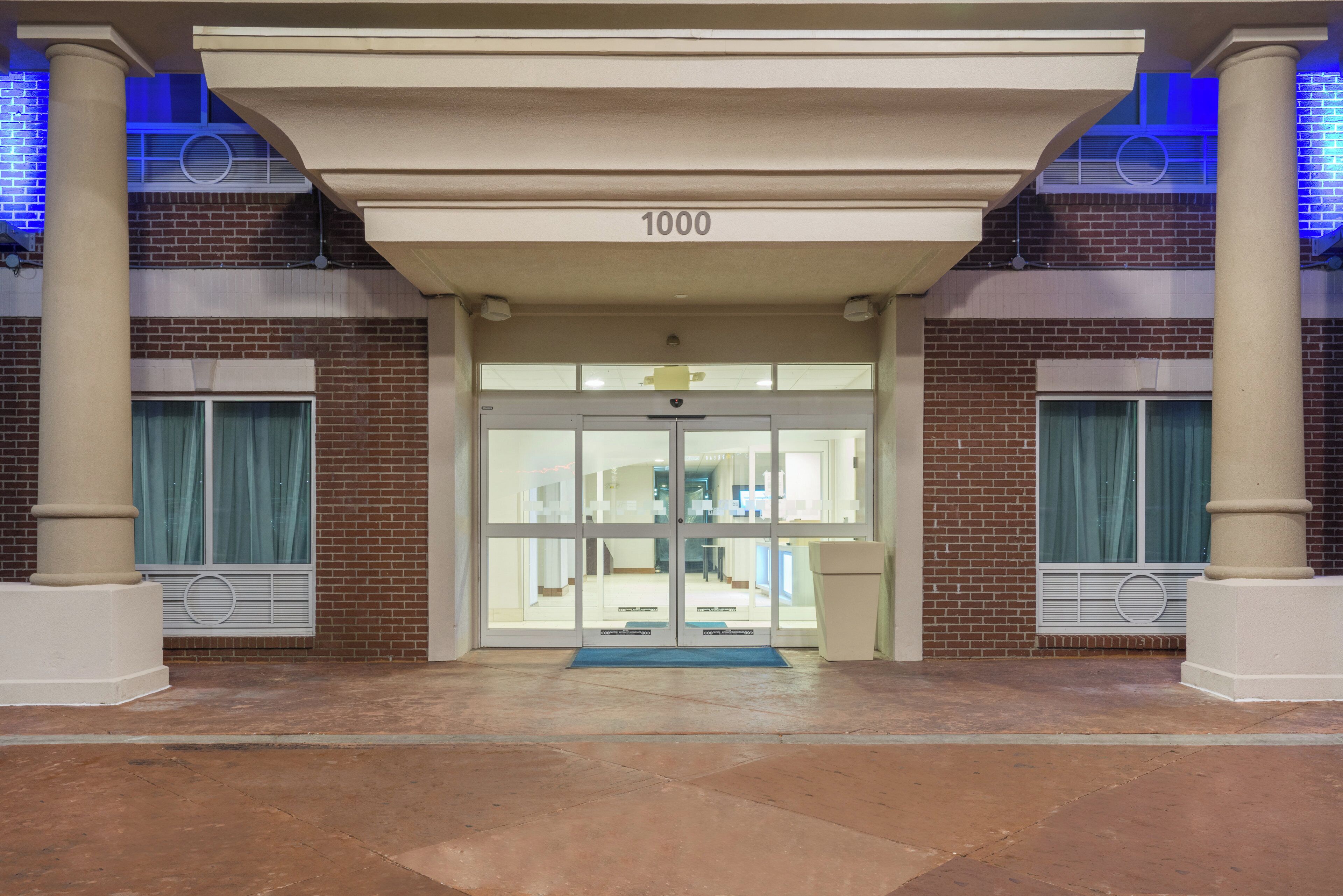 Una entrada de edificio con puerta de vidrio, el número '1000' en la parte superior y un felpudo azul en la entrada.