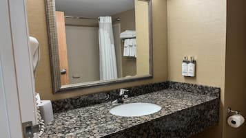 Une salle de bain avec un lavabo doté d’un plan de travail en granit, un grand miroir, un porte-serviettes avec des serviettes pliées et un distributeur de papier toilette.