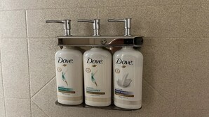 Tres productos Dove: champú, acondicionador y gel de baño, dispuestos en un estante con un grifo encima.