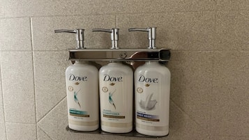 Drei Dove Produkte: Shampoo, Conditioner und Duschgel, angeordnet auf einem Regal mit einem Wasserhahn darüber.