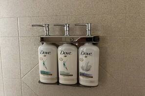 Drei Dove Produkte: Shampoo, Conditioner und Duschgel, angeordnet auf einem Regal mit einem Wasserhahn darüber.