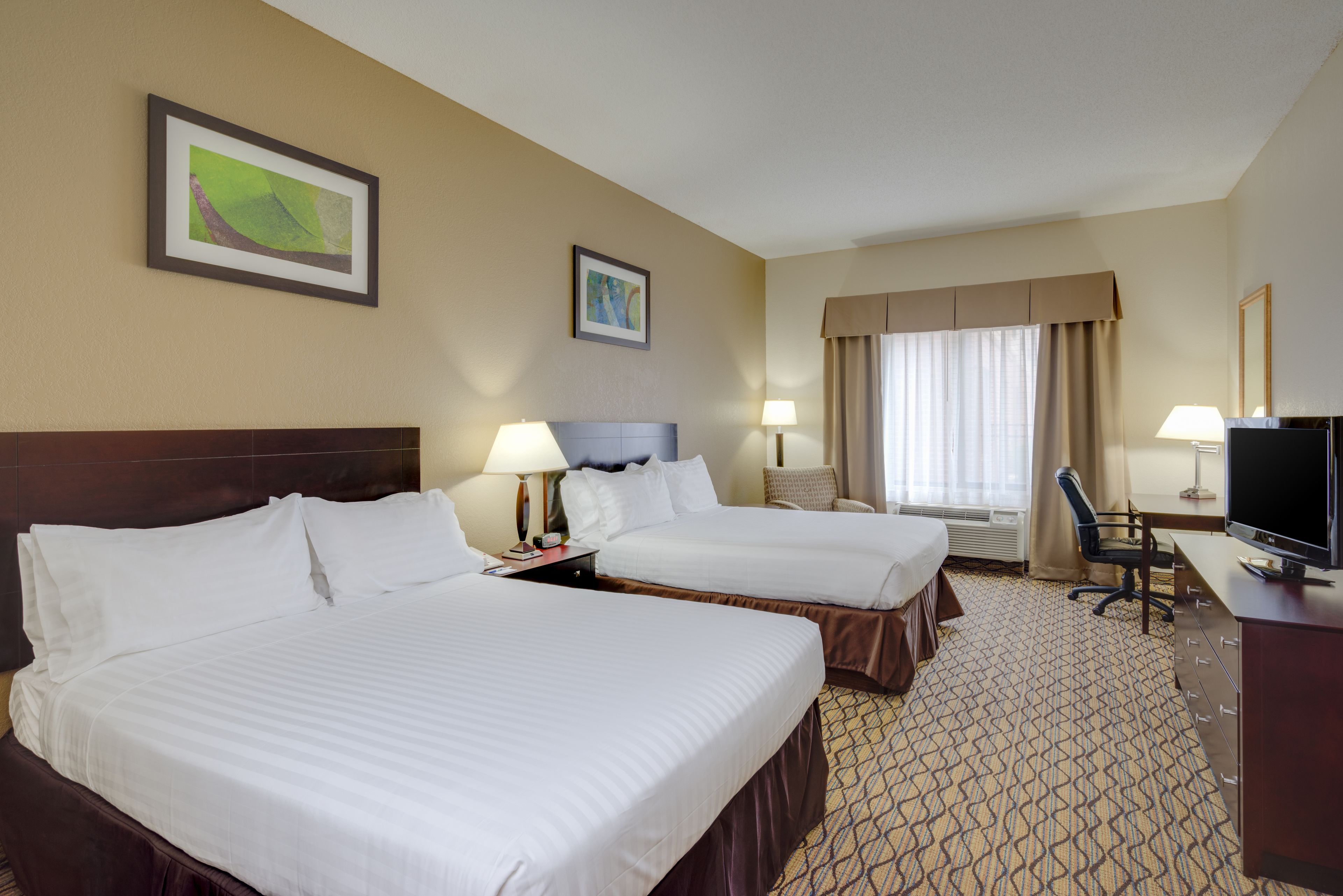 A hotel room with two beds, a desk, a TV, and two lamps.