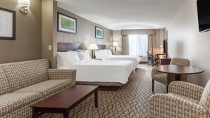 Habitación de hotel con una cama, dos mesitas de noche, un sofá, una silla, una pequeña mesa y un televisor.