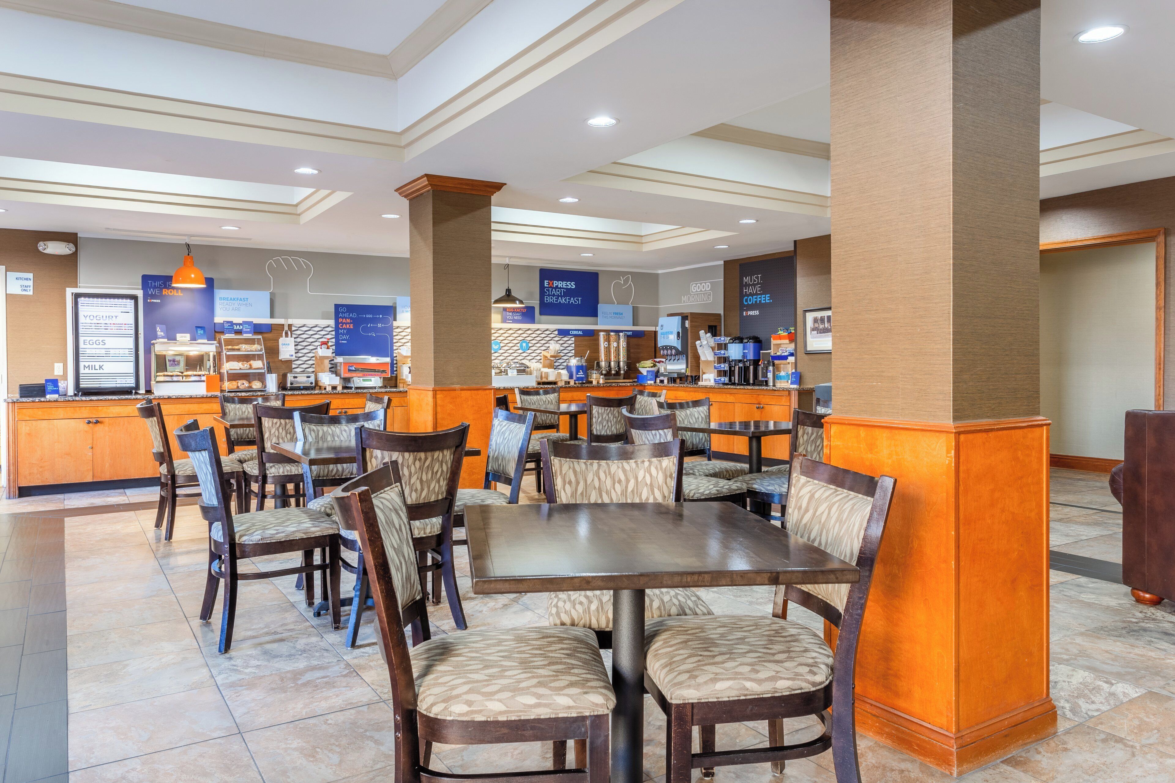 Un espace pour le petit-déjeuner à l’hôtel, comprenant un comptoir, des places assises et divers plats proposés au petit-déjeuner.