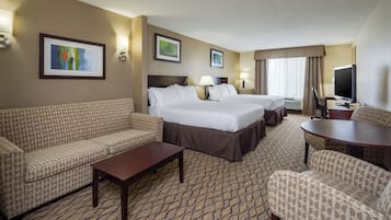 A hotel room with two beds, a sofa, a coffee table, a TV, and a patterned carpet.