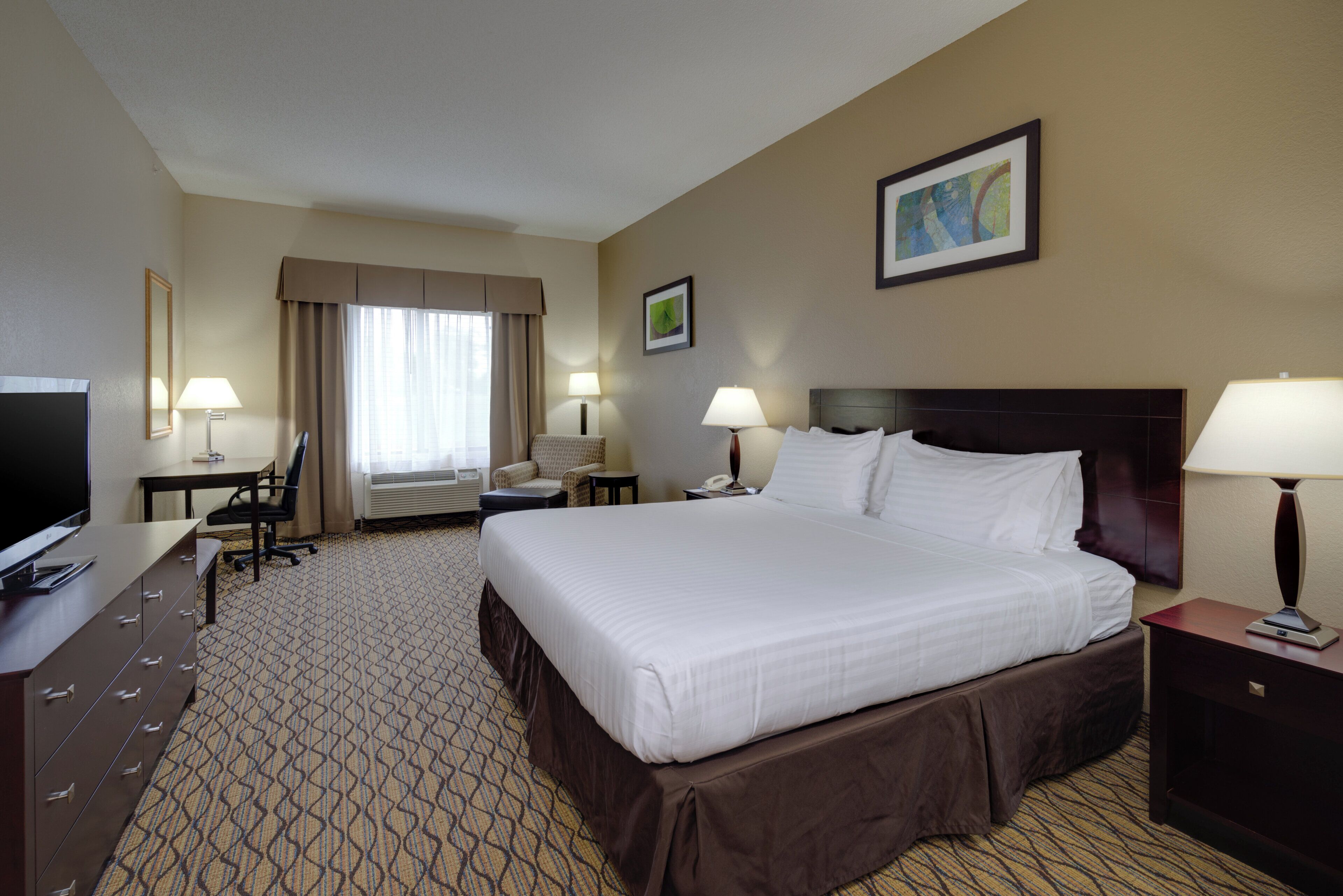 A hotel room with a large bed, a desk with a chair, a television, and two bedside lamps.