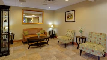 A hotel lobby with a sofa, two armchairs, a coffee table, a mirror, and a framed picture on the wall.