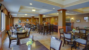 A hotel dining area with multiple tables and chairs, a television, and a coffee station. - Holiday Inn Express Charles Town by IHG (Charles Town)