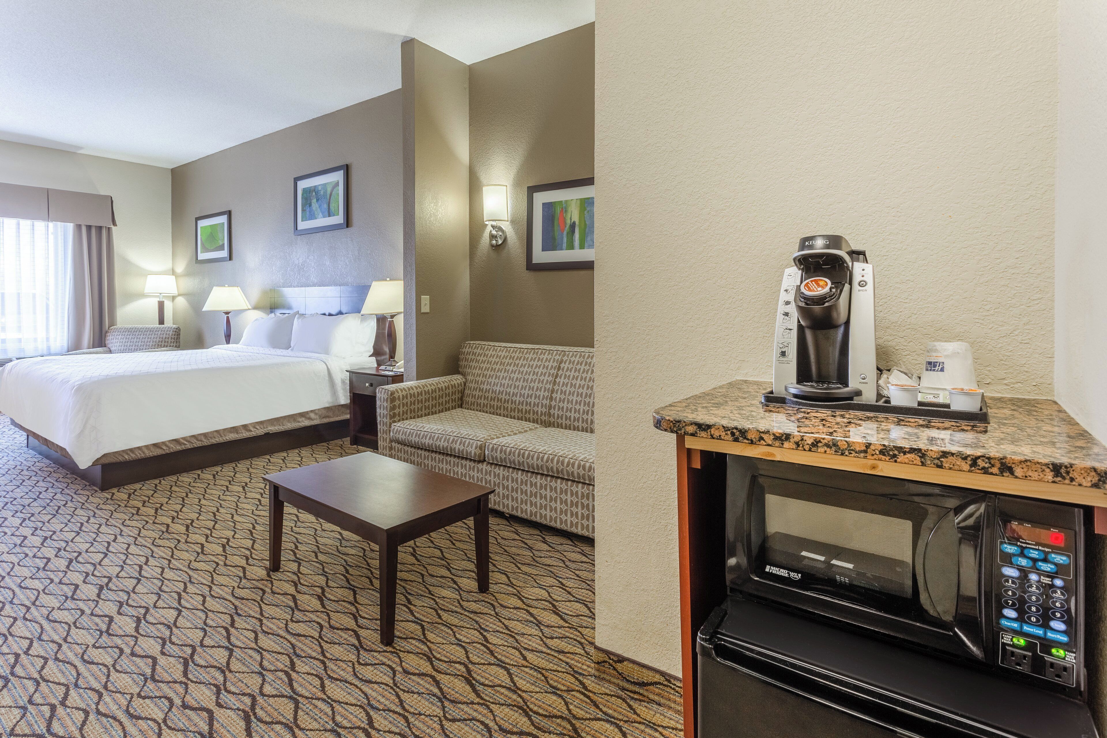 A hotel room with a bed, a sofa, a small table, a microwave, and a coffee maker.