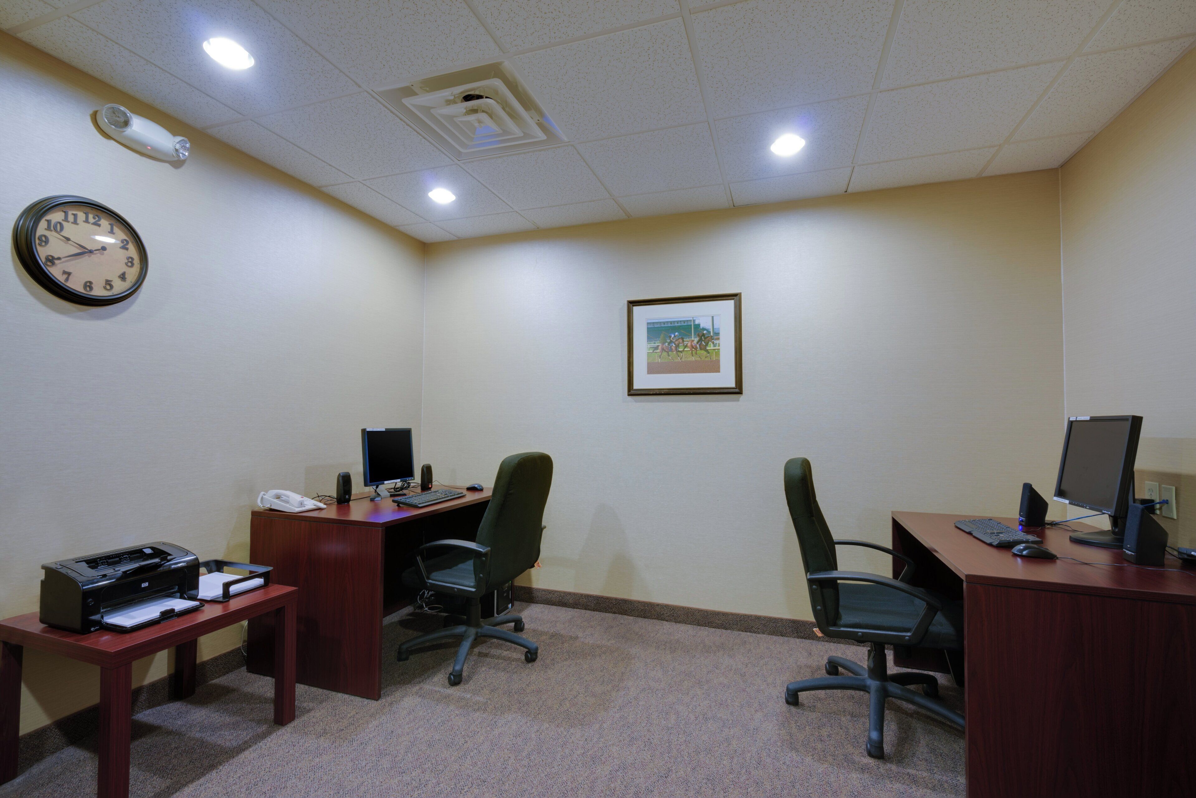 A conference room with two desks, chairs, a clock, and a framed picture on the wall.