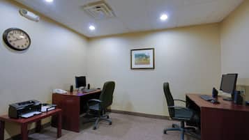 A conference room with two desks, chairs, a clock, and a framed picture on the wall.