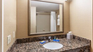 Un baño con encimera de granito, un lavamanos blanco, un espejo y un perchero para toallas.