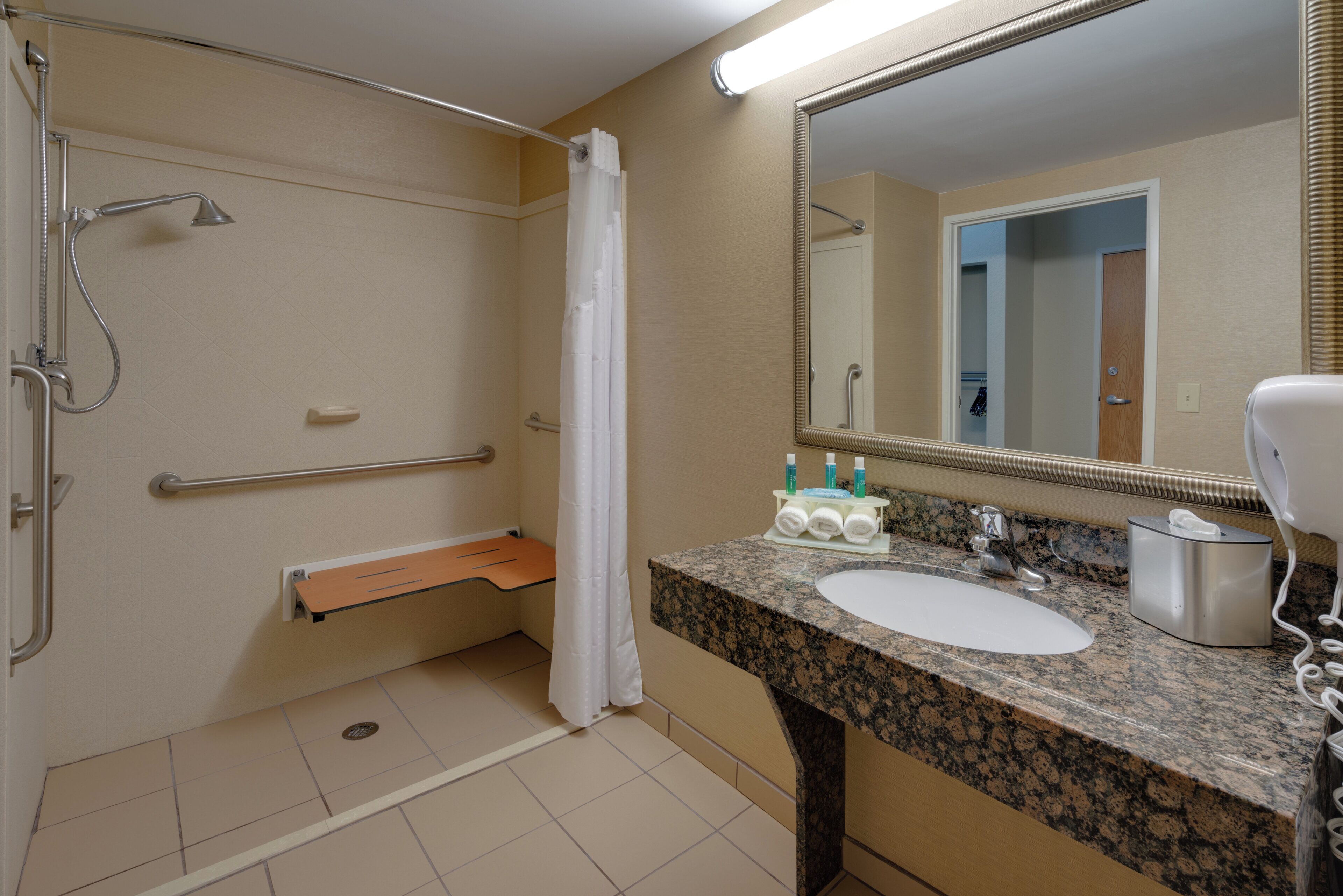 Une salle de bain équipée d’une douche, d’une barre d’appui, d’un porte-serviettes, d’un lavabo et d’un miroir.