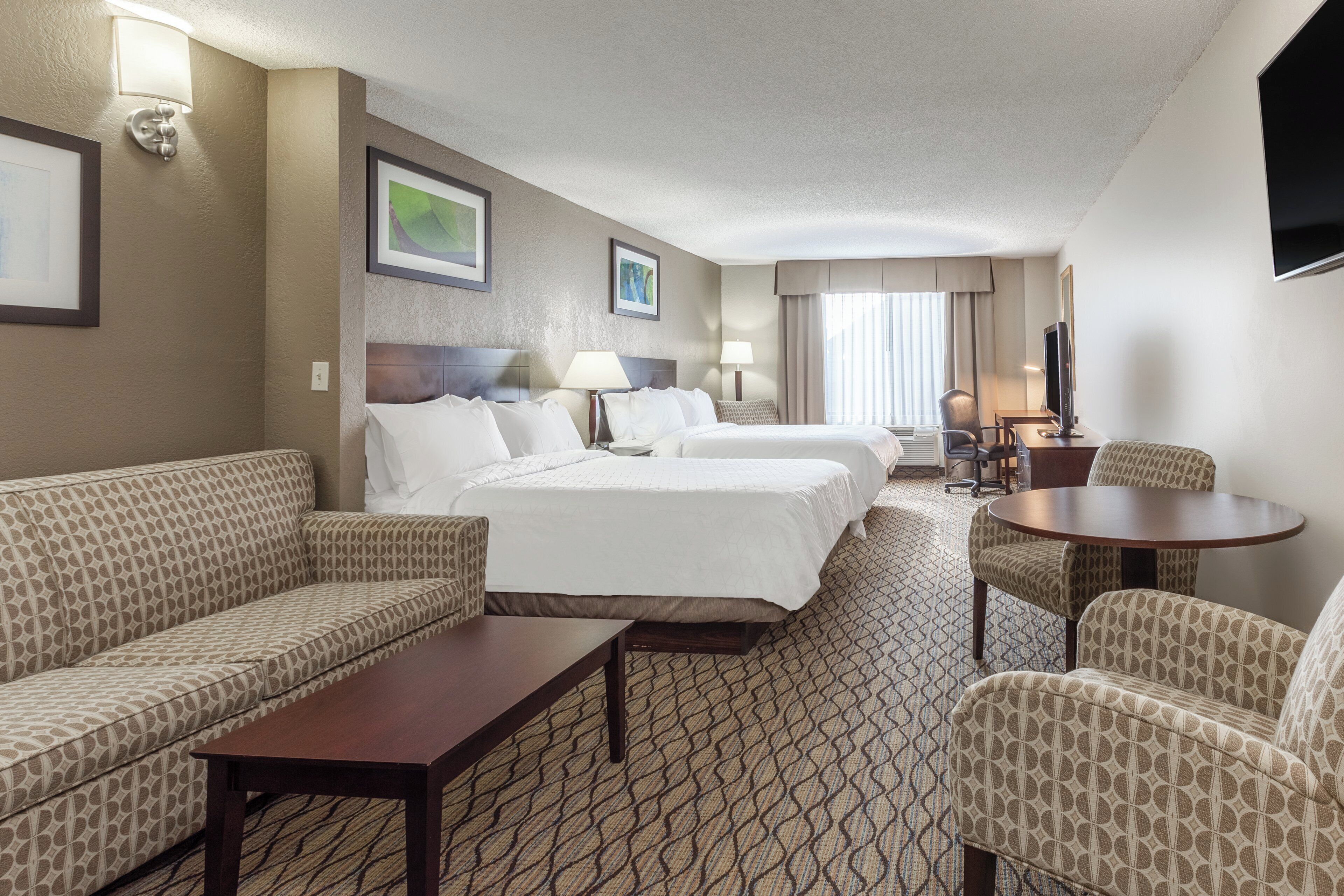 Une chambre d’hôtel comprenant un lit, deux tables de chevet, un canapé, un fauteuil et un téléviseur.