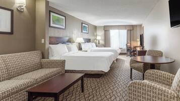 Une chambre d’hôtel comprenant un lit, deux tables de chevet, un canapé, un fauteuil et un téléviseur.