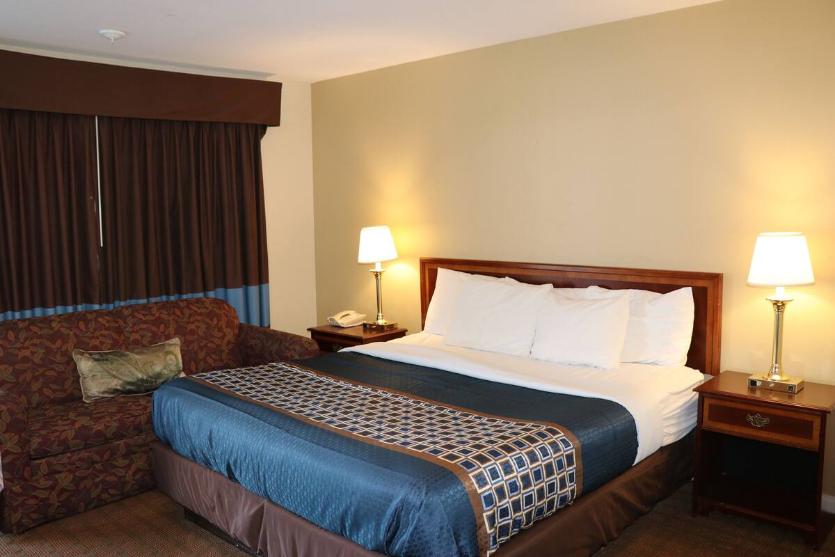 A hotel room with a large bed, a sofa, two bedside tables with lamps, and a window with curtains.