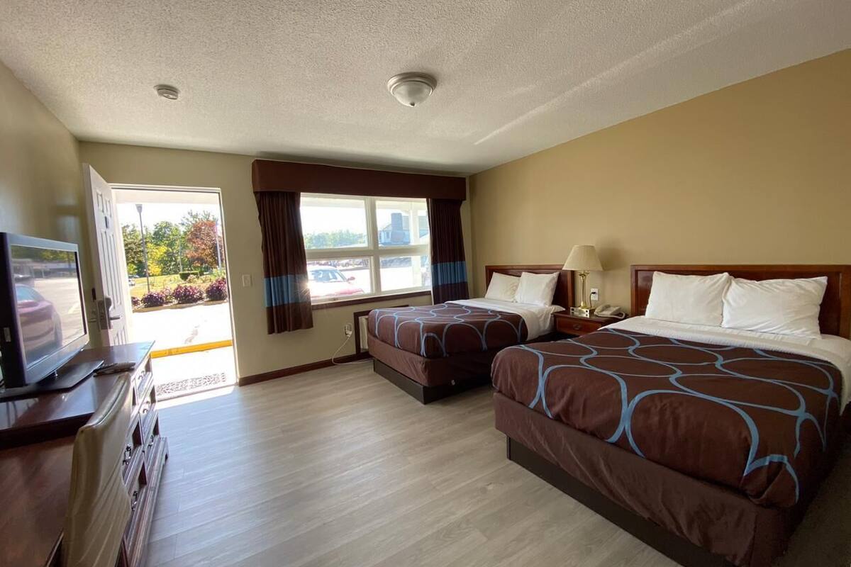 A hotel room with two beds, a TV, a desk, and a window with curtains.