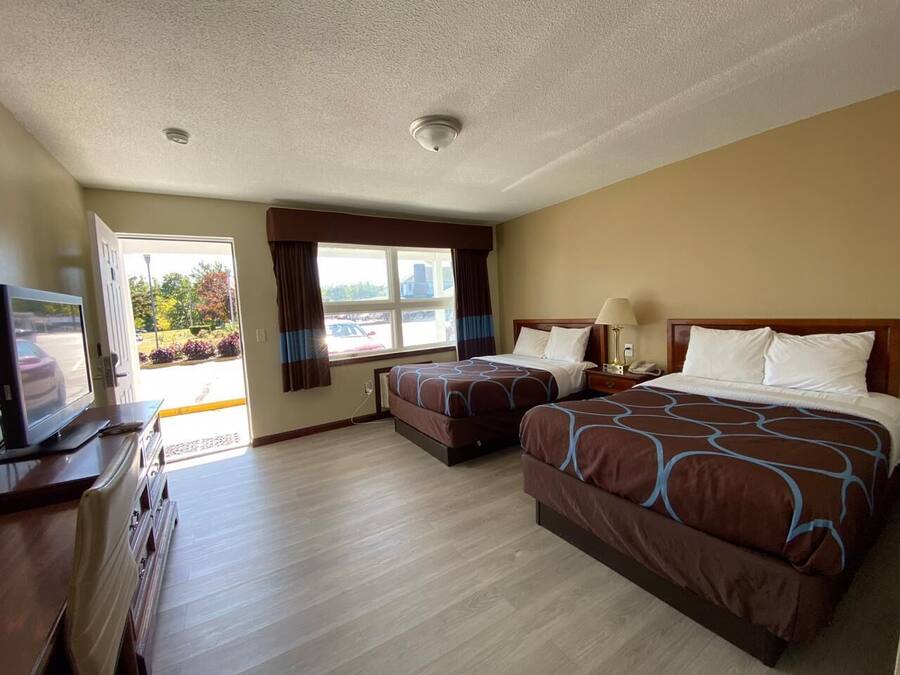 A hotel room with two beds, a TV, a desk, and a window with curtains.