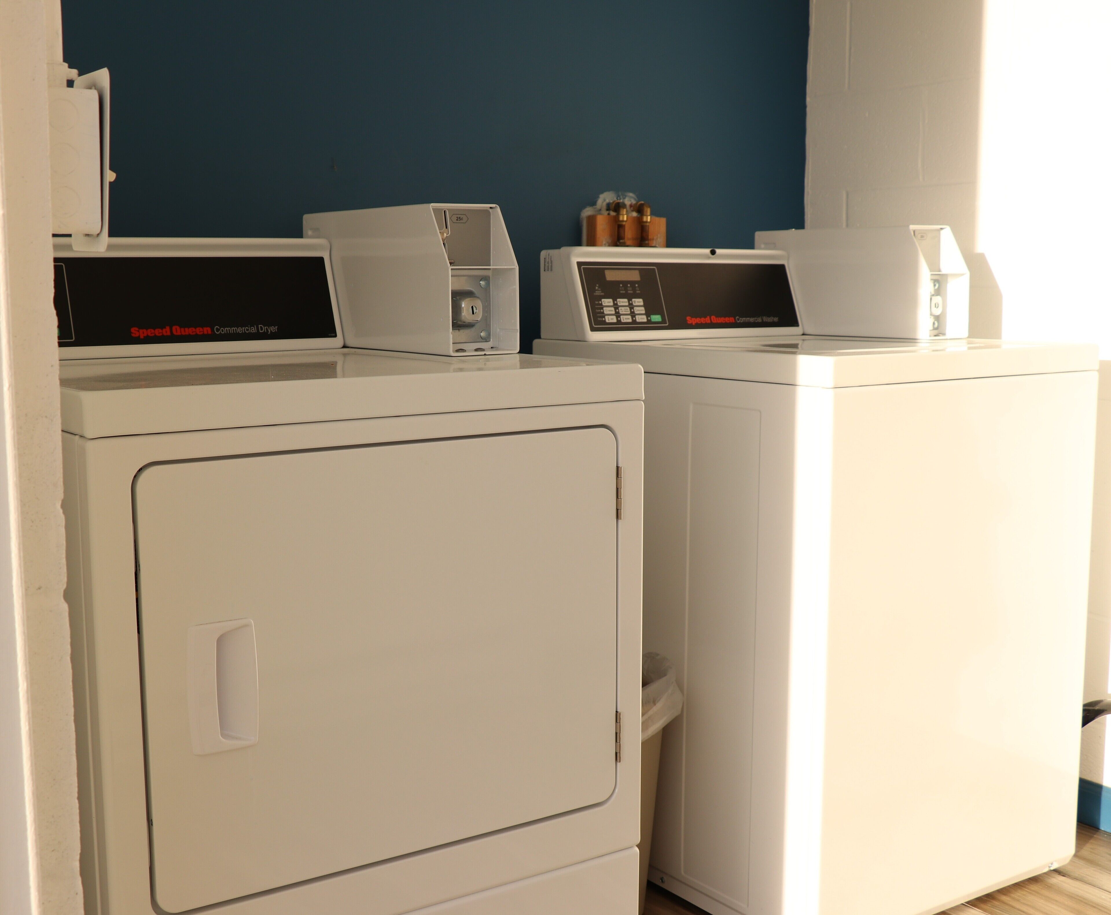 A laundry area with two white commercial dryers, one with a control panel and the other with a digital display.