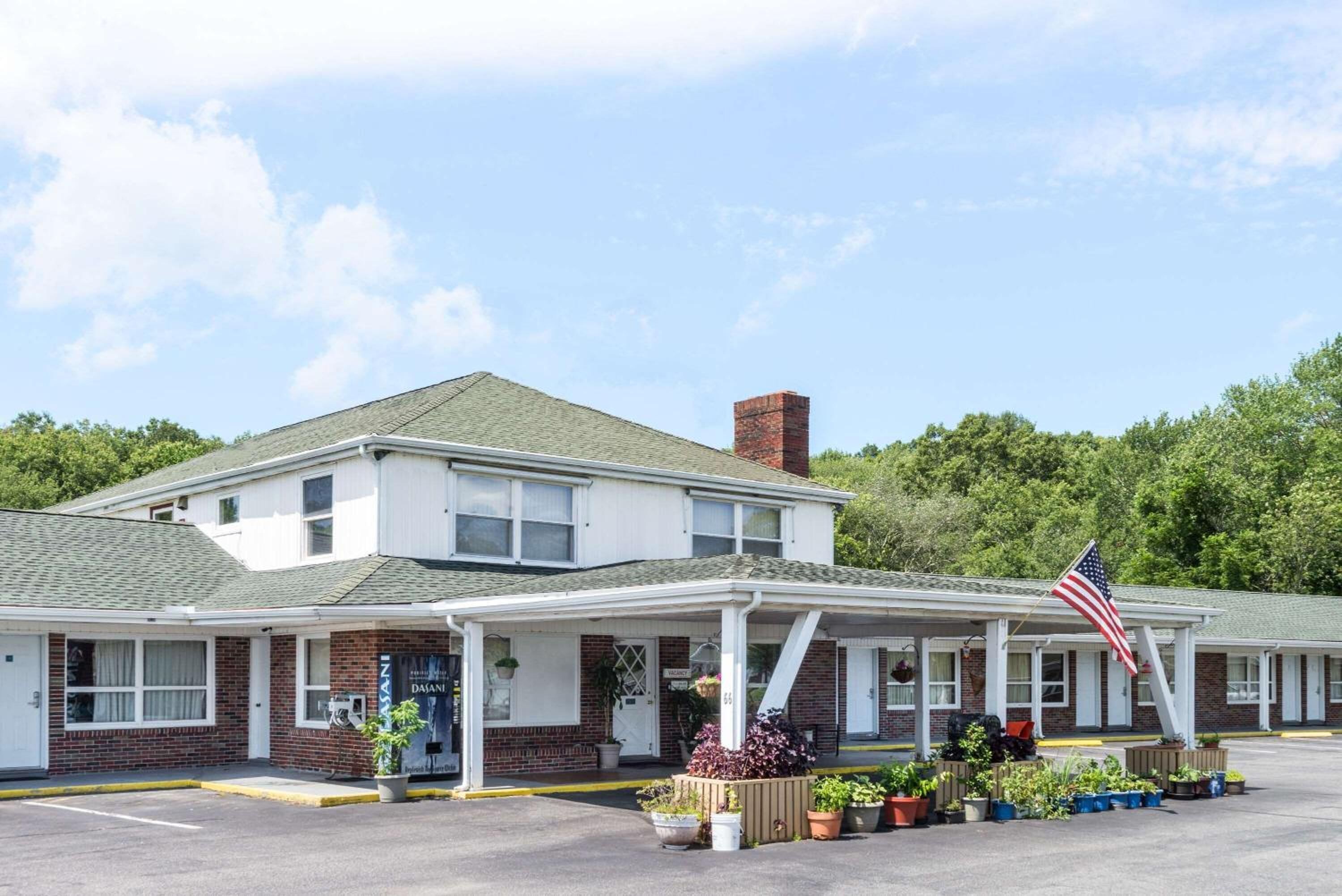A motel with a covered front porch, a brick facade, and an American flag.