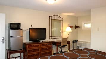 A hotel room with a bed, a television, a refrigerator, a desk, a chair, a lamp, and a mirror.