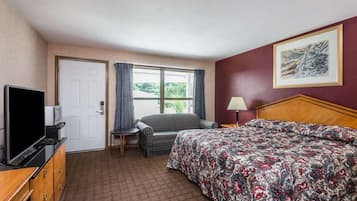 A hotel room with a bed, a TV, a desk, a chair, a window with curtains, and a painting on the wall.