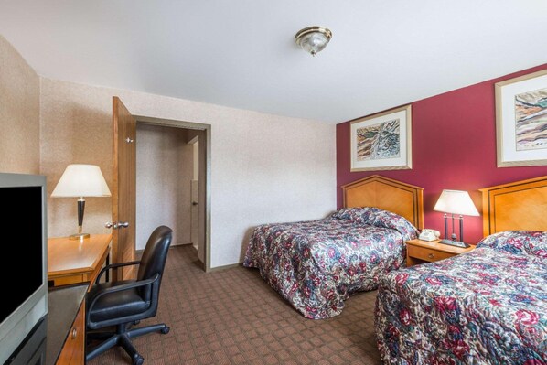 Habitación de hotel con dos camas, un escritorio con silla, un televisor y una puerta que da a otra habitación.