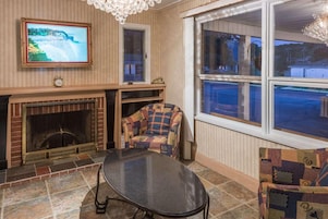 Una sala de estar con chimenea, un televisor montado en la pared, un sillón estampado y un ventanal con vistas al exterior.