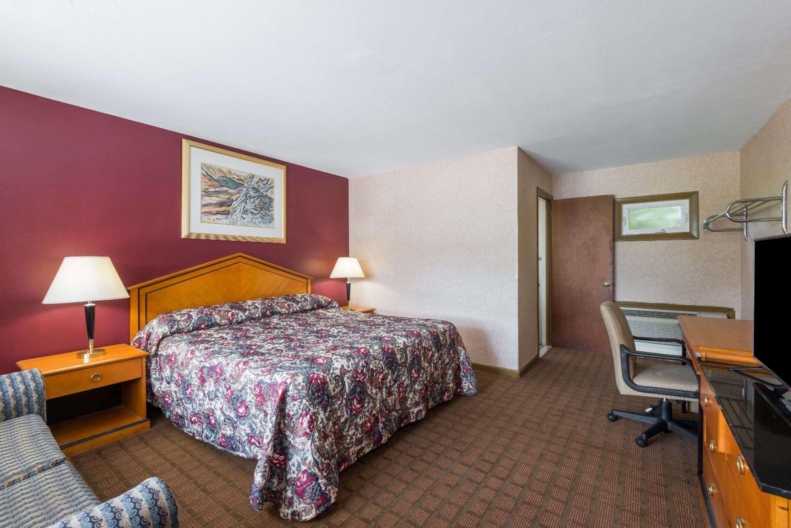 Habitación de hotel con cama, dos lámparas de noche, un escritorio con silla, televisión y un cuadro en la pared.
