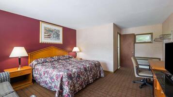 A hotel room with a bed, two bedside lamps, a desk with a chair, a television, and a framed picture on the wall.