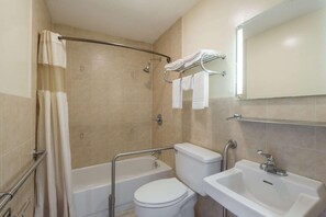 A bathroom with a bathtub, toilet, and sink, equipped with grab bars and a towel rack.