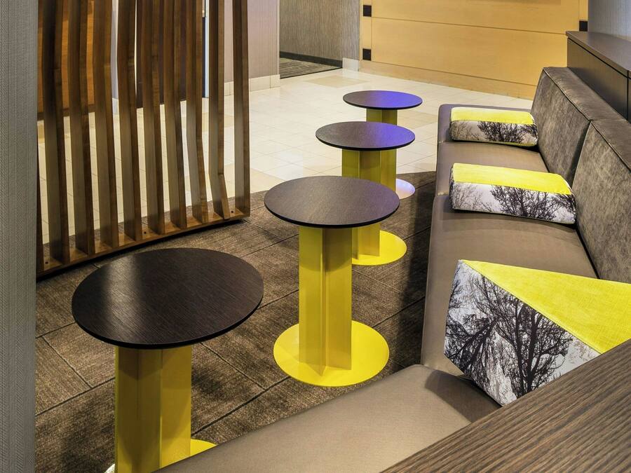 A modern lobby with a curved ceiling, a seating area with sofas and round tables, a flat-screen TV, and a wall with abstract art.