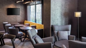 A modern lounge area with multiple seating options, including sofas and chairs, arranged around a central table. A flat-screen TV is mounted on the wall, and there is a floor lamp providing additional lighting. - SpringHill Suites by Marriott Bakersfield (Bakersfield)