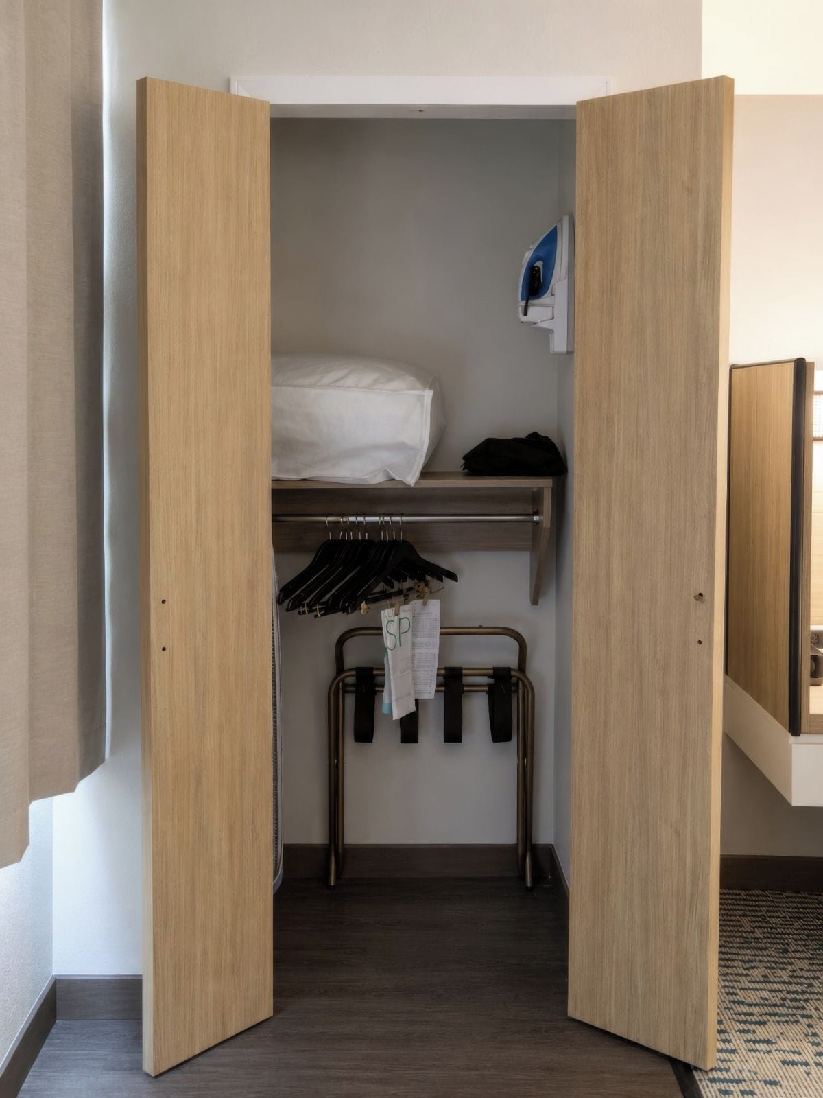 A compact room with a bed, a shelf, a hanging rack, and a small table.