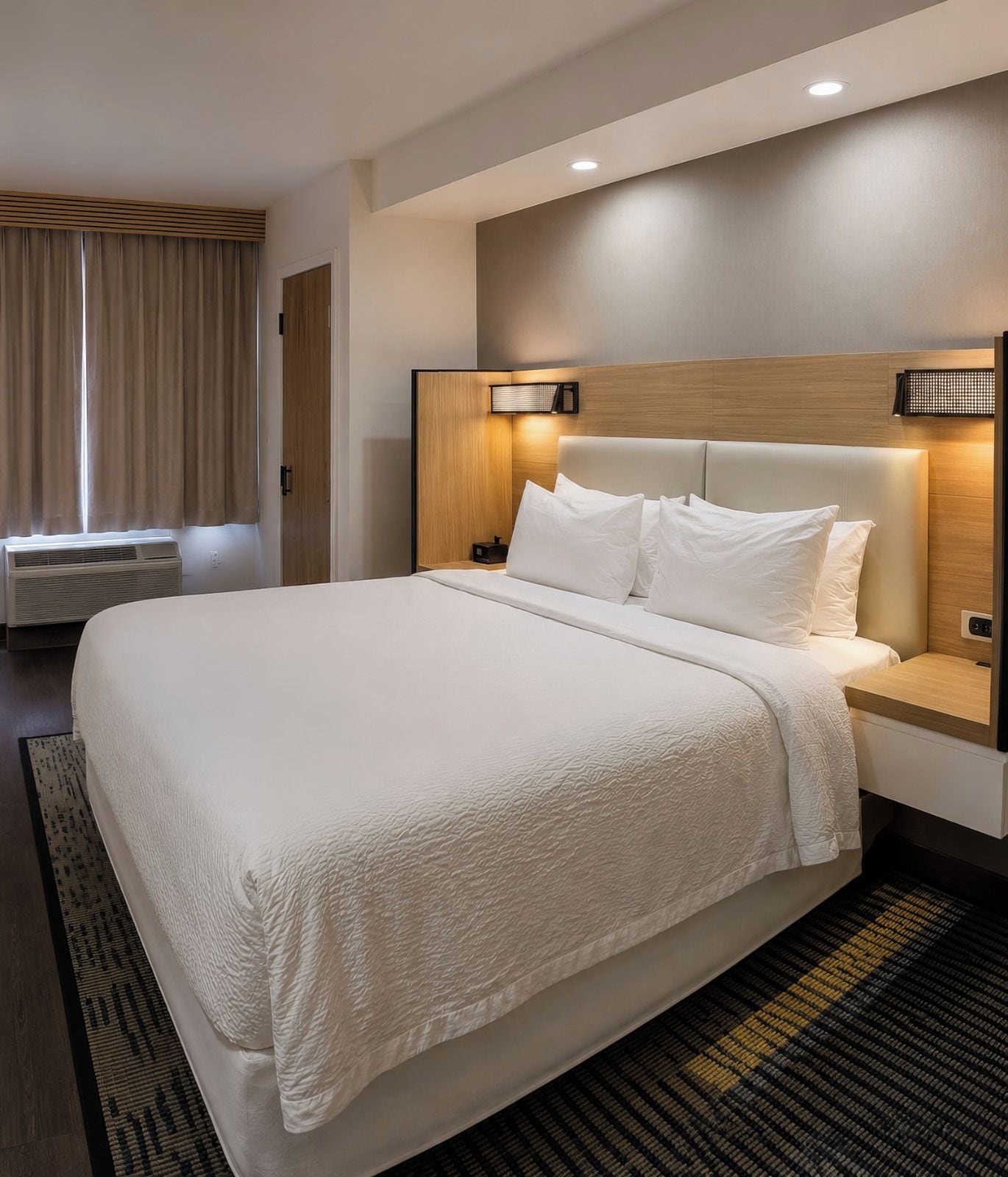 Una habitación de hotel con una cama grande, cabecera de madera, lámparas de noche y una ventana con cortinas.