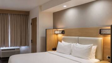 Una habitación de hotel con una cama grande, cabecera de madera, lámparas de noche y una ventana con cortinas.