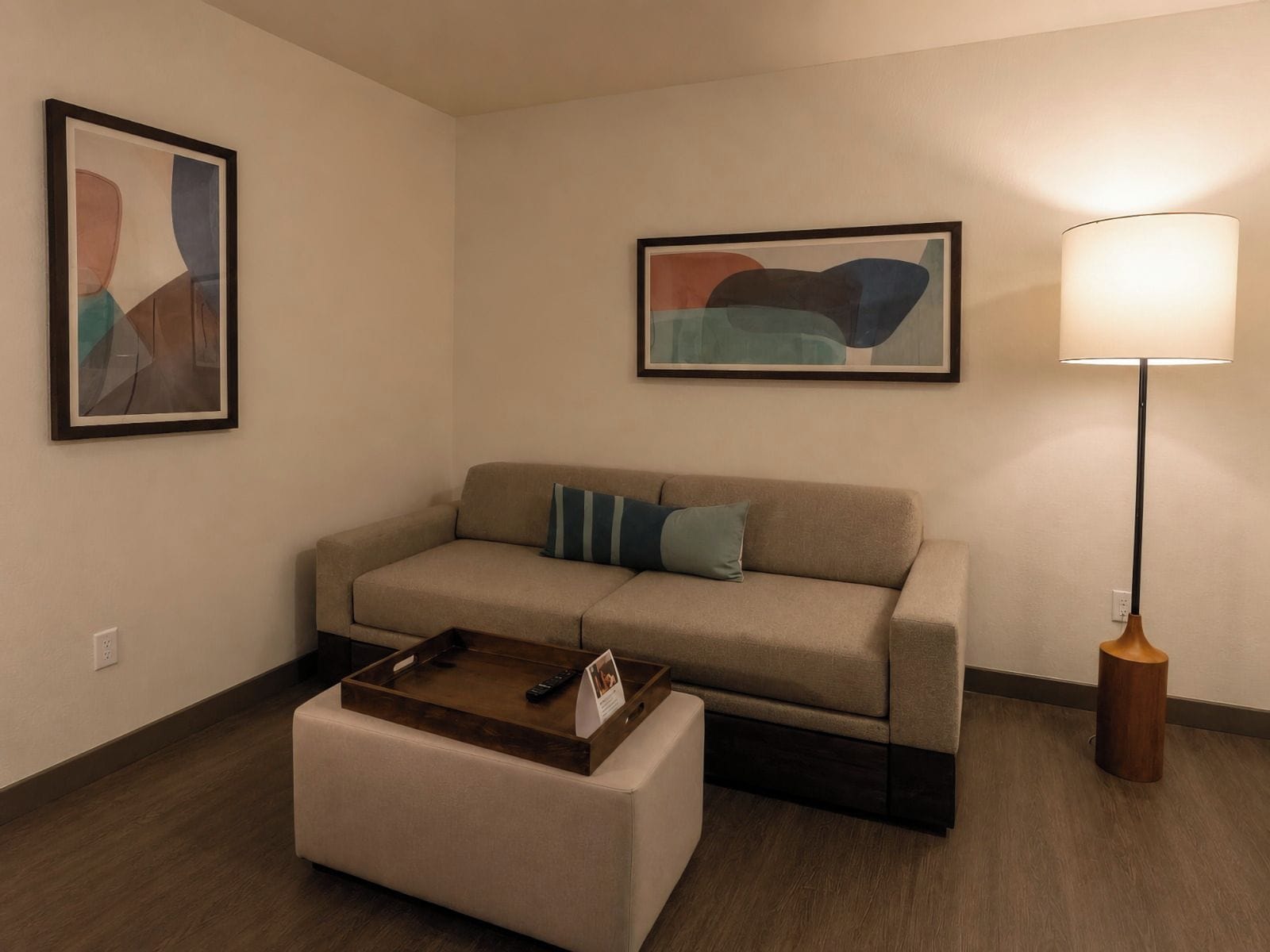 A neutral-colored sofa with a tray table and pillows, a standing floor lamp, and abstract artwork on the walls.