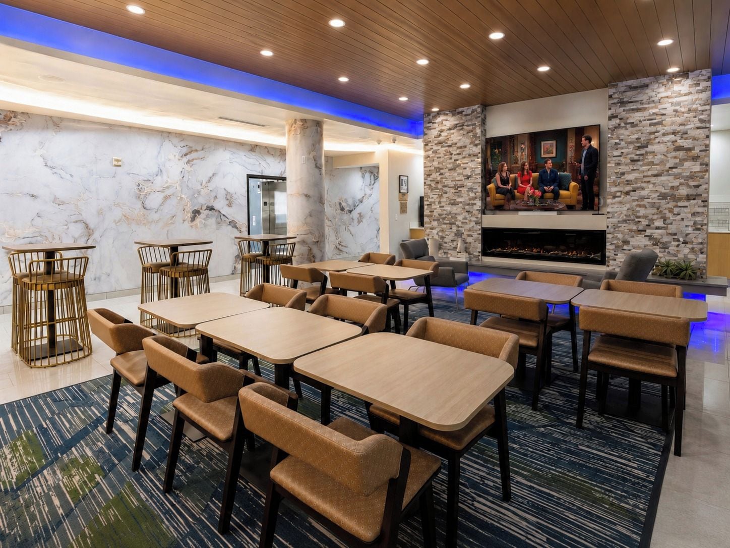 A modern lounge area with marble walls, a stone accent wall, and a fireplace. Tables and chairs are arranged for guests.