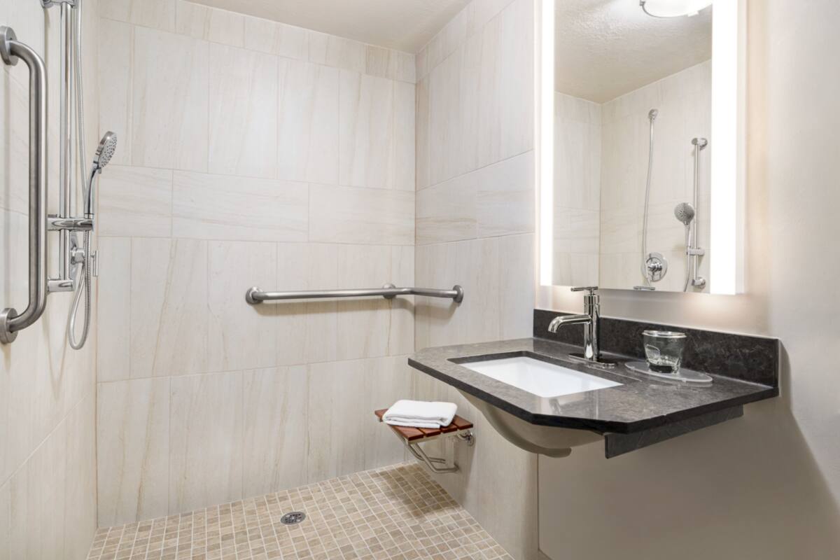 A modern bathroom with a shower, grab bar, sink, and a glass of water on the counter.