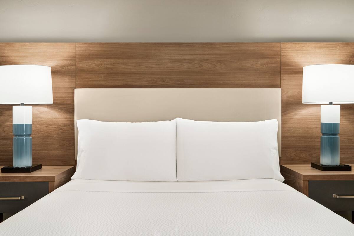 A neatly made bed with white linens, flanked by two bedside tables with lamps, set against a wooden headboard.