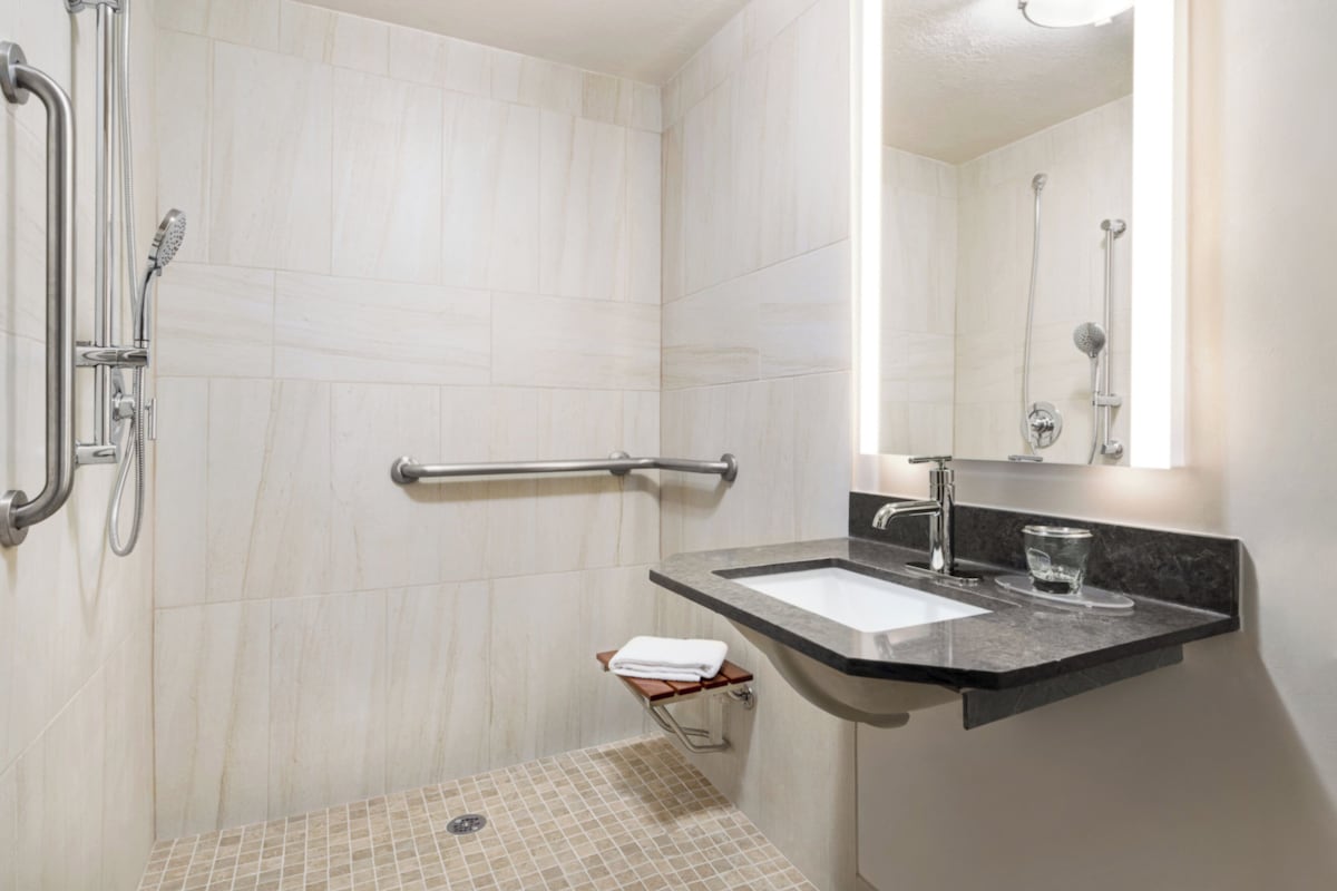 A modern bathroom with a shower, grab bar, sink, and a glass of water on the counter.