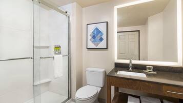 Un baño moderno con cabina de ducha de vidrio, inodoro blanco, lavabo con espejo y una obra de arte enmarcada en la pared.
