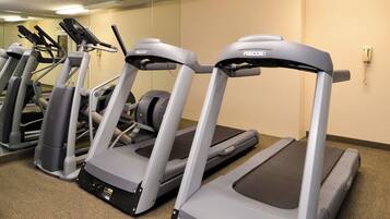 A row of treadmills in a gym with a beige wall and carpeted floor.
